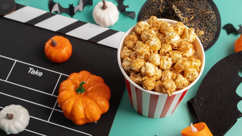 halloween themed movie night scene with popcorn, pumpkins, and bats on a teal background