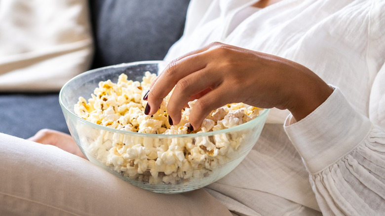 Woman sits on her sofa and eats popcorn from a glass bowl