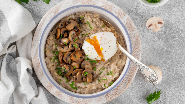 Savory oatmeal with a broken hard boiled egg, mushrooms, and a green garnish inside a bowl with a spoon.