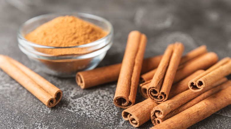 pile of cinnamon sticks next to small bowl of ground cinnamon