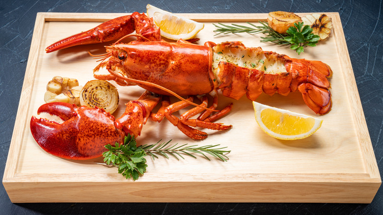 Cooked whole lobster on a wooden board with lemon and herbs