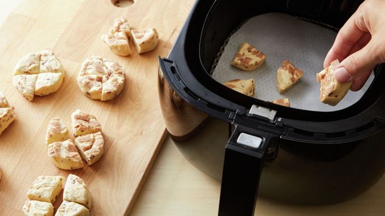 Unbaked cinnamon rolls cut into fours being placed inside an air fryer basket