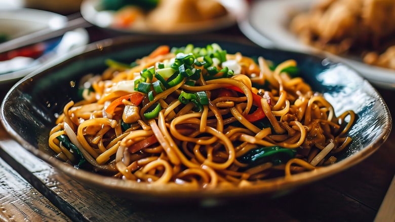 A black bowl of chow mein noodles on a brown wooden table.