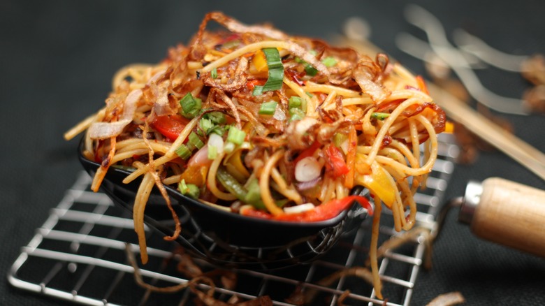 chow mein noodles overflowing in a black bowl.