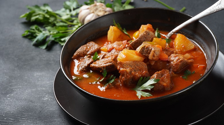 Bowl of beef stew next to some herbs