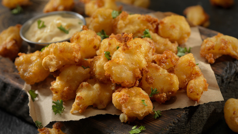 Plate of fried cheese curds with garnish on top and a ramekin of dipping sauce