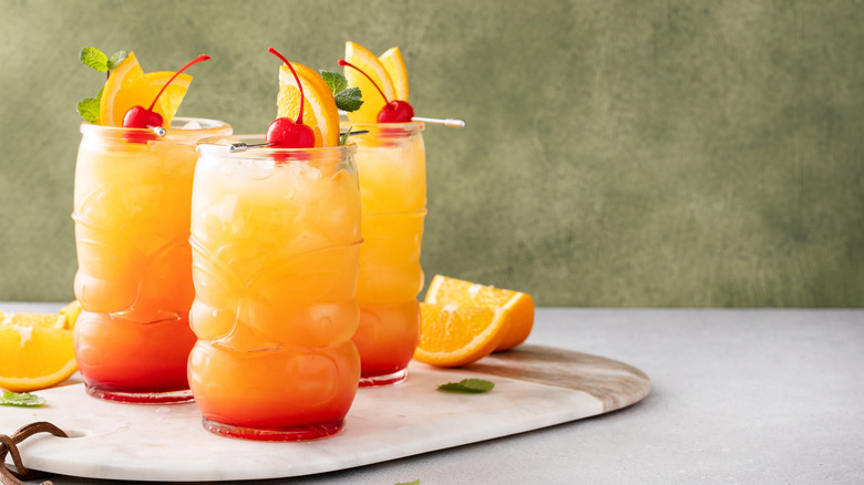 Three glass cups full of rum punch with cherries, orange slices, and mint garnish.