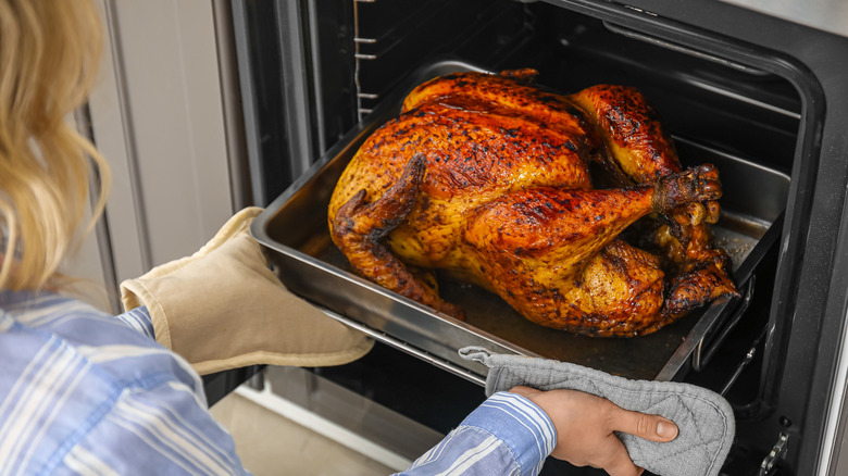 A blonde woman taking a turkey out of the oven