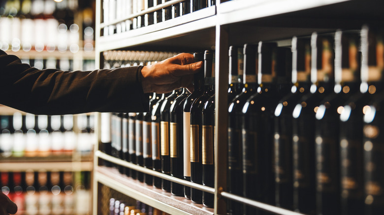 person choosing a bottle of wine on shelf