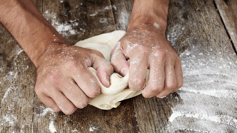 A person's hands kneading dough on a wooden surface