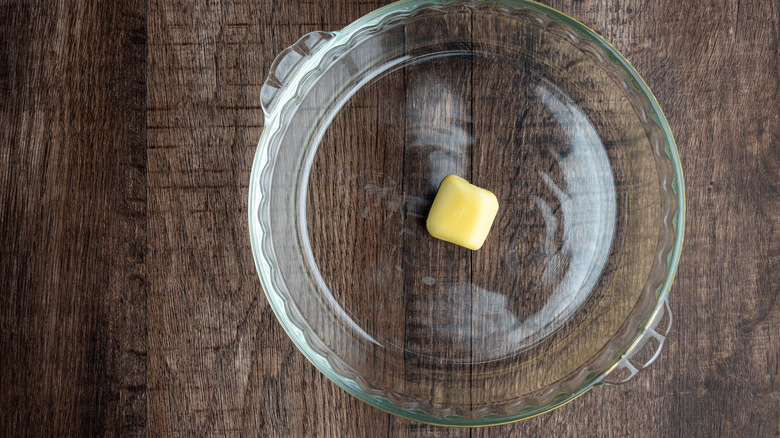 A glass pie pan with a pat of butter in it