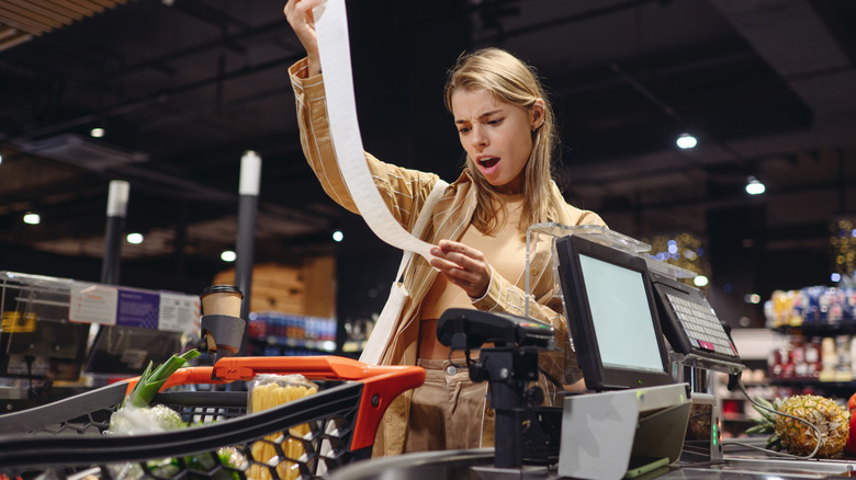 A person shocked by their receipt at a grocery store checkout counter