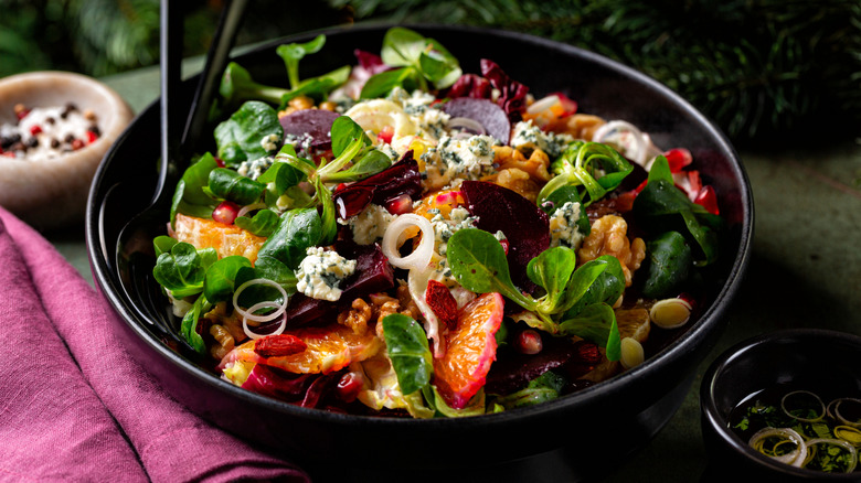 Salad in a black bowl with black utensils and a pink cloth napkin