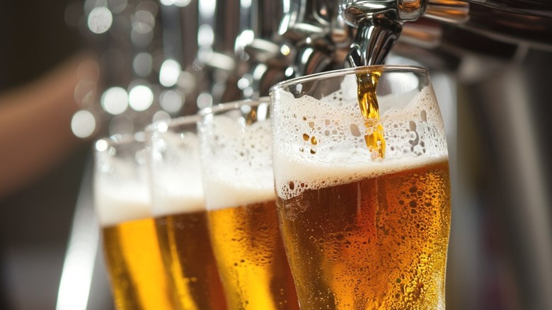 Three glasses of beer being poured from tap.