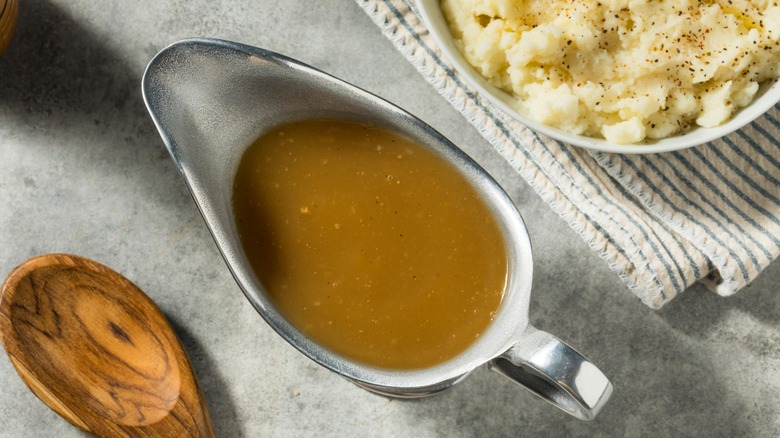 metal gravy boat of brown gravy alongside wooden spoon and mashed potatoes