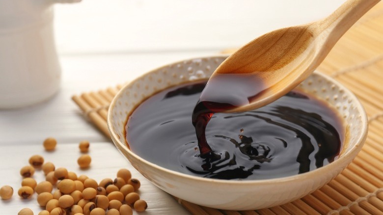 A bowl of soy sauce with a wooden spoon and dry soybeans on the side