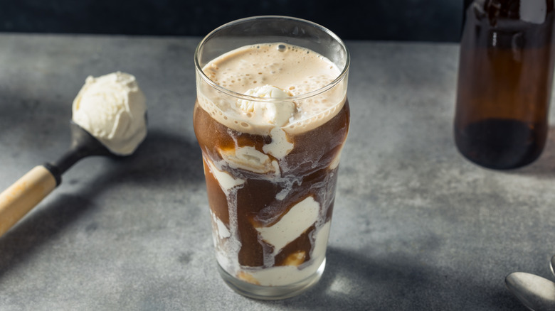 A root beer and vanilla ice cream float in a pint glass with a scoop of vanilla ice cream in the background