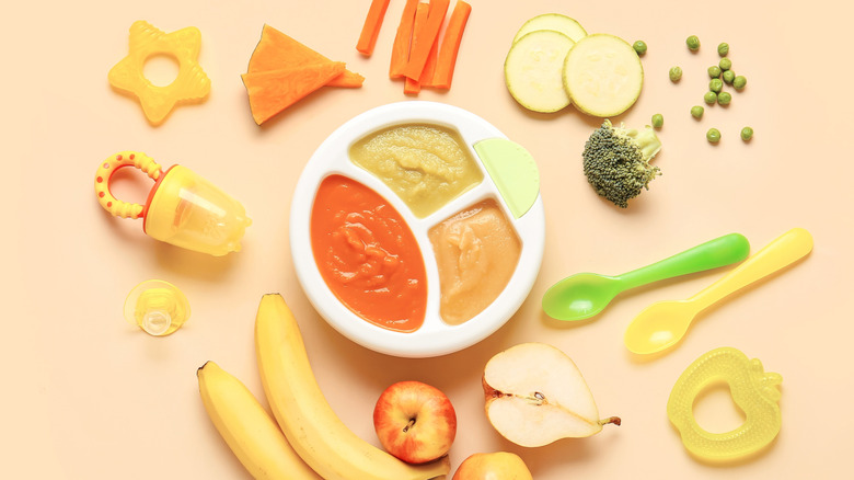 A container of baby food surrounded by raw fruits and vegetables