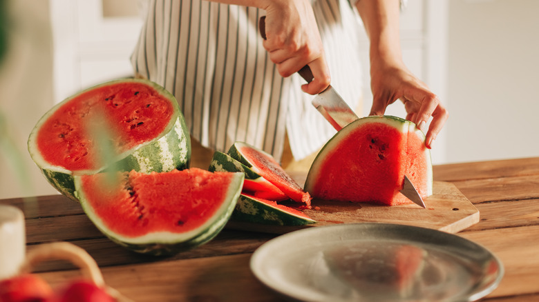 Woman cutting watermelon into pieces on cutting board