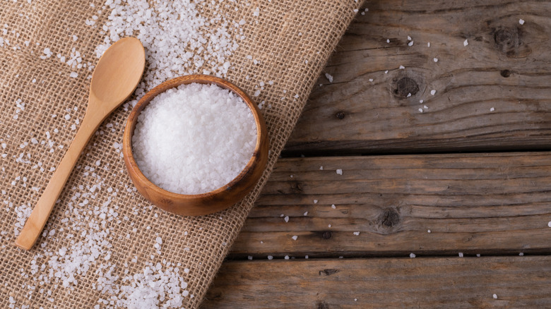 A wooden bowl of rock salt on a wooden table