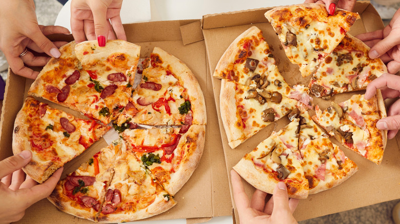 People helping themselves to sliced pizza.