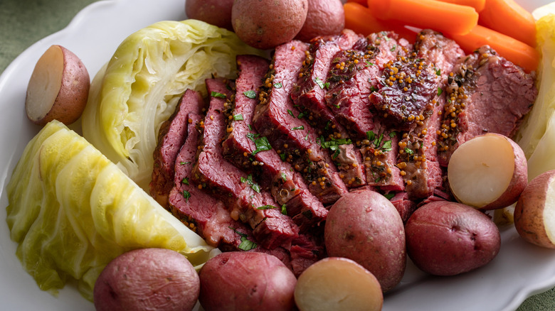 corned beef with cabbage, boiled potatoes, and carrots on a white platter