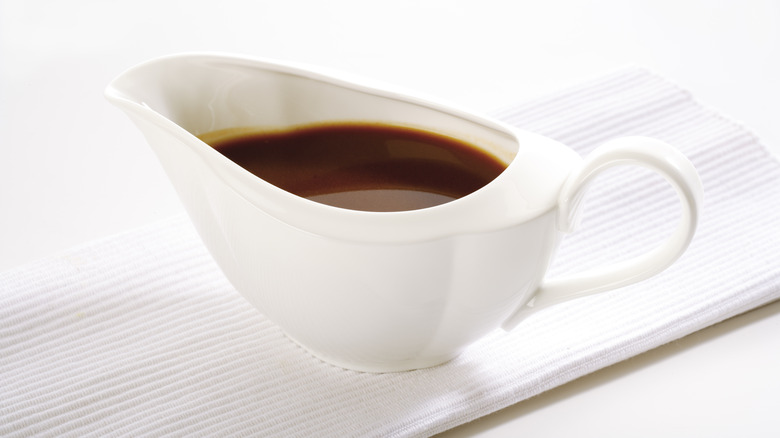 brown gravy inside a white gravy boat in front of a white background