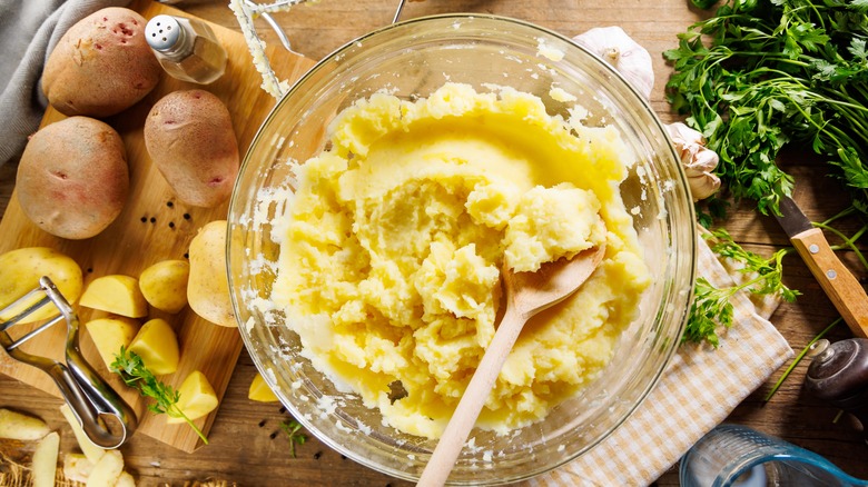 mashed potatoes in a bowl with potatoes and herbs around