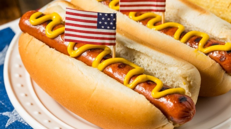 A pair of hot dogs drizzled with mustard, with American flags sticking out of them.