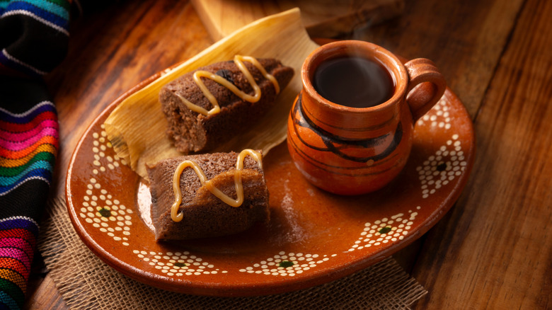 A chocolate tamale with caramel drizzle on a plate next to a cup of coffee