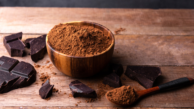 Ground cocoa powder in a wooden bowl next to chocolate bar chunks