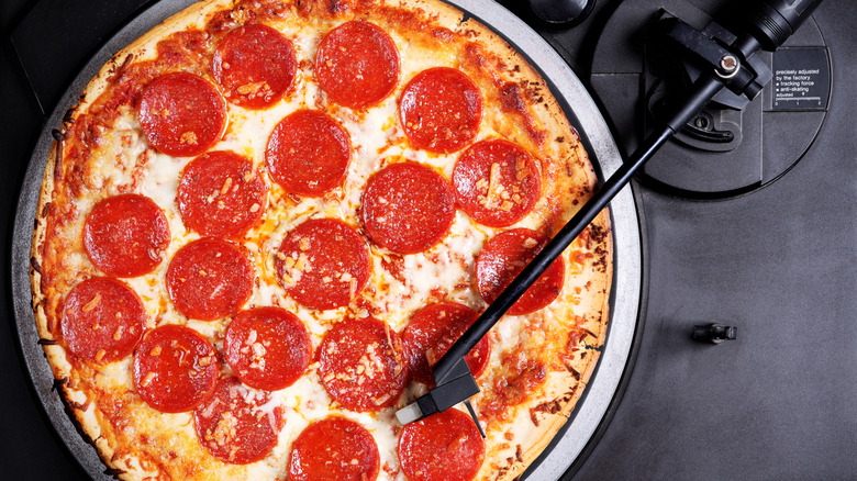 A record player's tonearm rests on a pepperoni pizza lying on its turntable