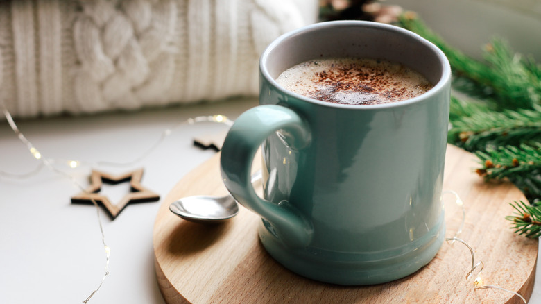 Hot chocolate in a mug on top of a wooden table next to a spoon.