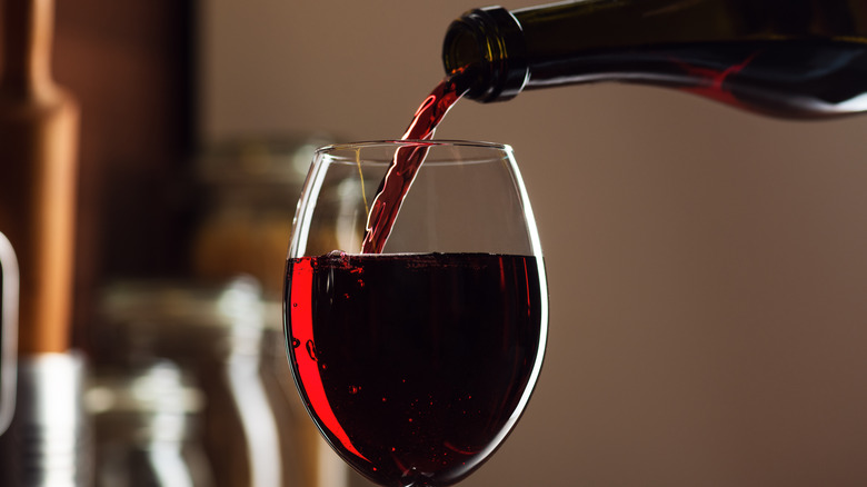 A bottle of red wine pouring into a glass.