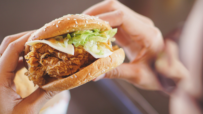 Holding a fried chicken sandwich with lettuce and cheese