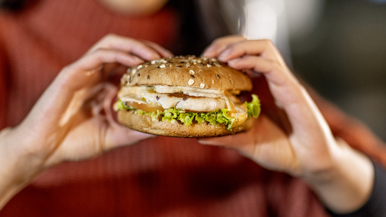 Woman in red sweater holds a fast food grilled chicken sandwich