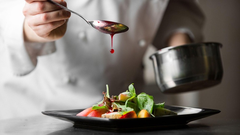 Chef drizzling sauce on colorful plated dish