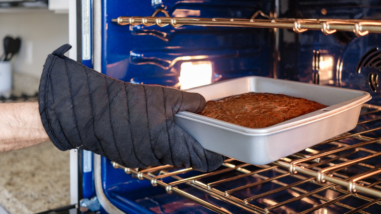 Hand in oven mitttaking finished brownie batter out of oven