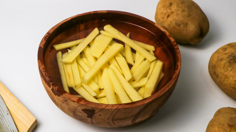 Raw, sliced potatoes in a bowl of water with whole potatoes