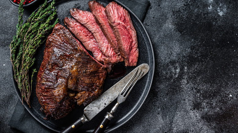 Hanger steak on a black plate with a knife, fork, and herb garnish