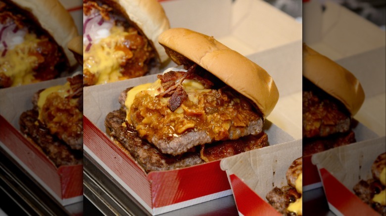 A Wendy's baconator cheeseburger with chili on it in a cardboard box.