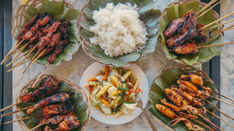 plates of Filipino barbecue skewers on banana leaves with rice and veggies