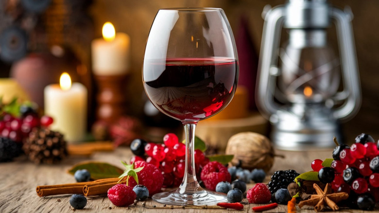 A glass of red wine on a table beside grapes, cranberries and candles