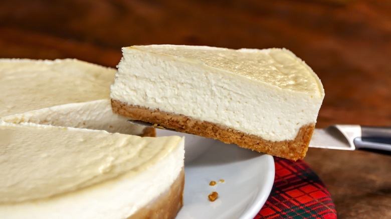 A slice of plain white cheesecake being cut from a whole cake