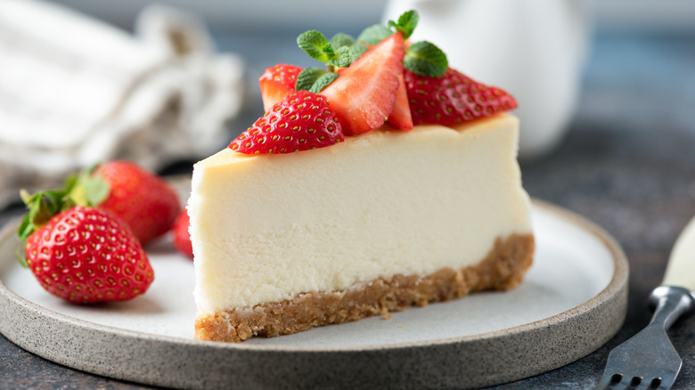 A slice of New York style cheesecake topped with fresh strawberries