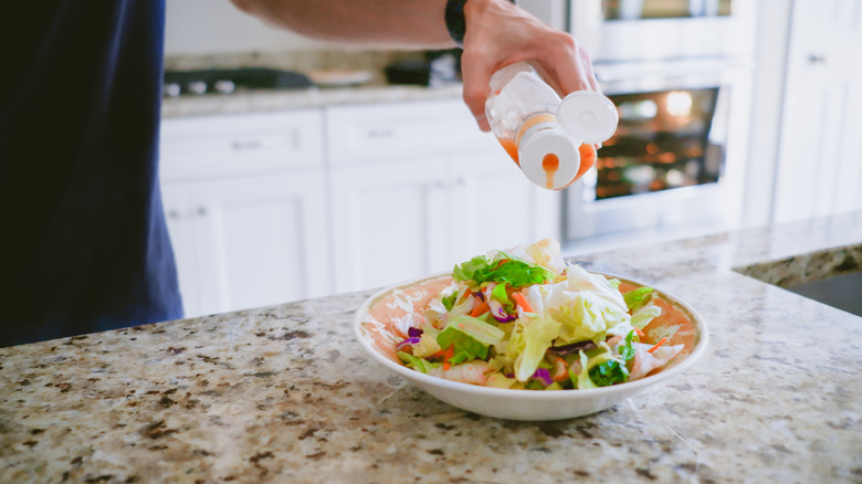 a man pouring salad dressing from a bottle onto a salad