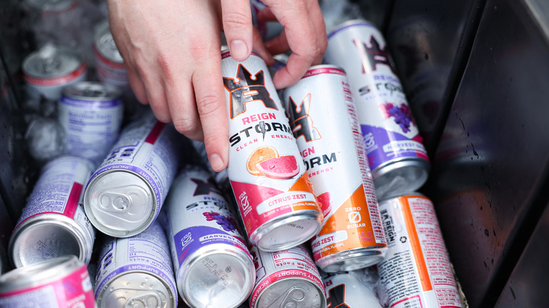 A person taking from a pile of energy drink cans.