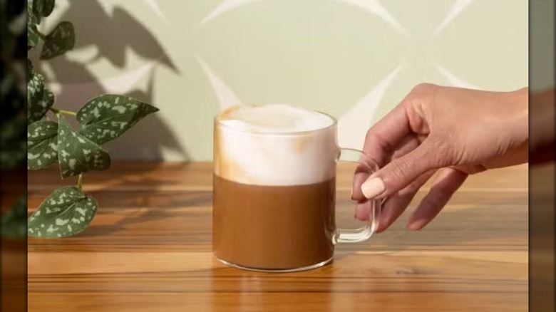 Hand reaching for glass coffee cup containing caffe misto