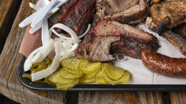 Pickles and raw onions served on a platter of barbecue meats