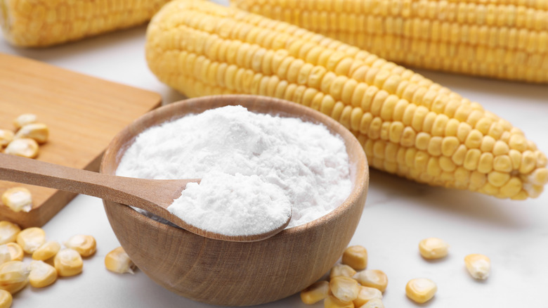 A wooden bowl of cornstarch with whole corn and kernels behind it